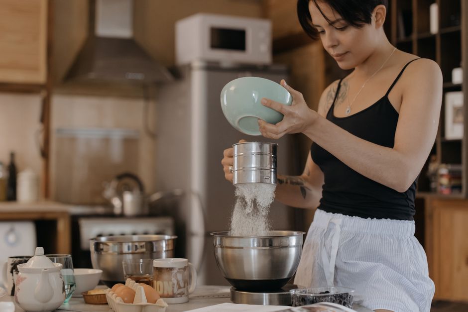 A woman sifts flour into a bowl in a cozy kitchen. Culinary preparation at home.