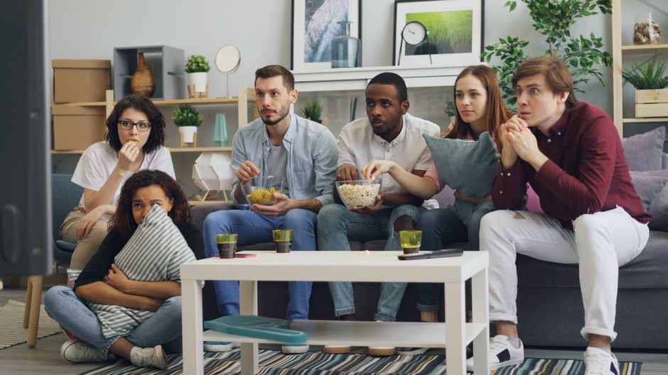 Group of friends watching a movie on a couch, enjoying snacks and drinks indoors.